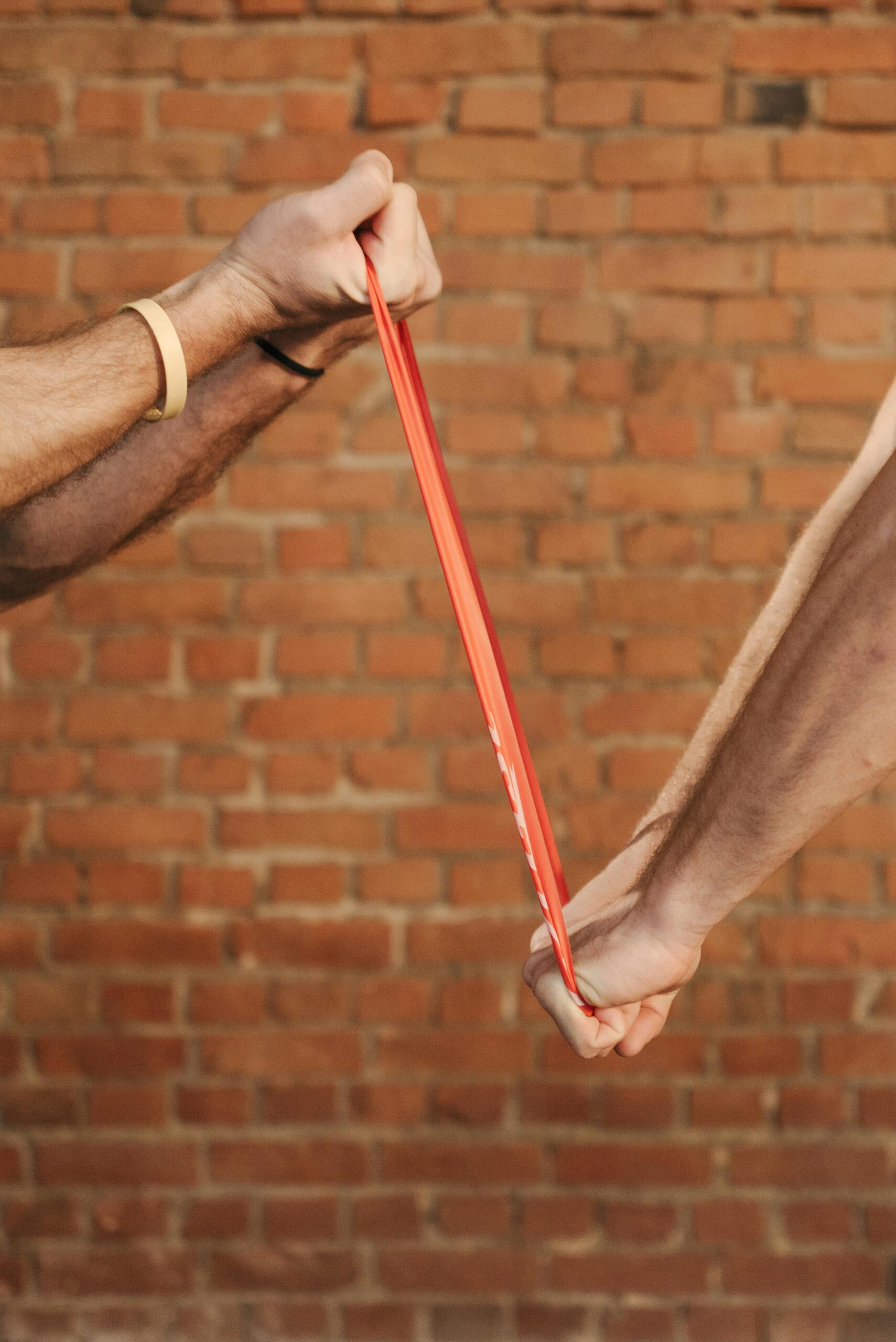 Two people exercising with a resistance band against a brick wall background.