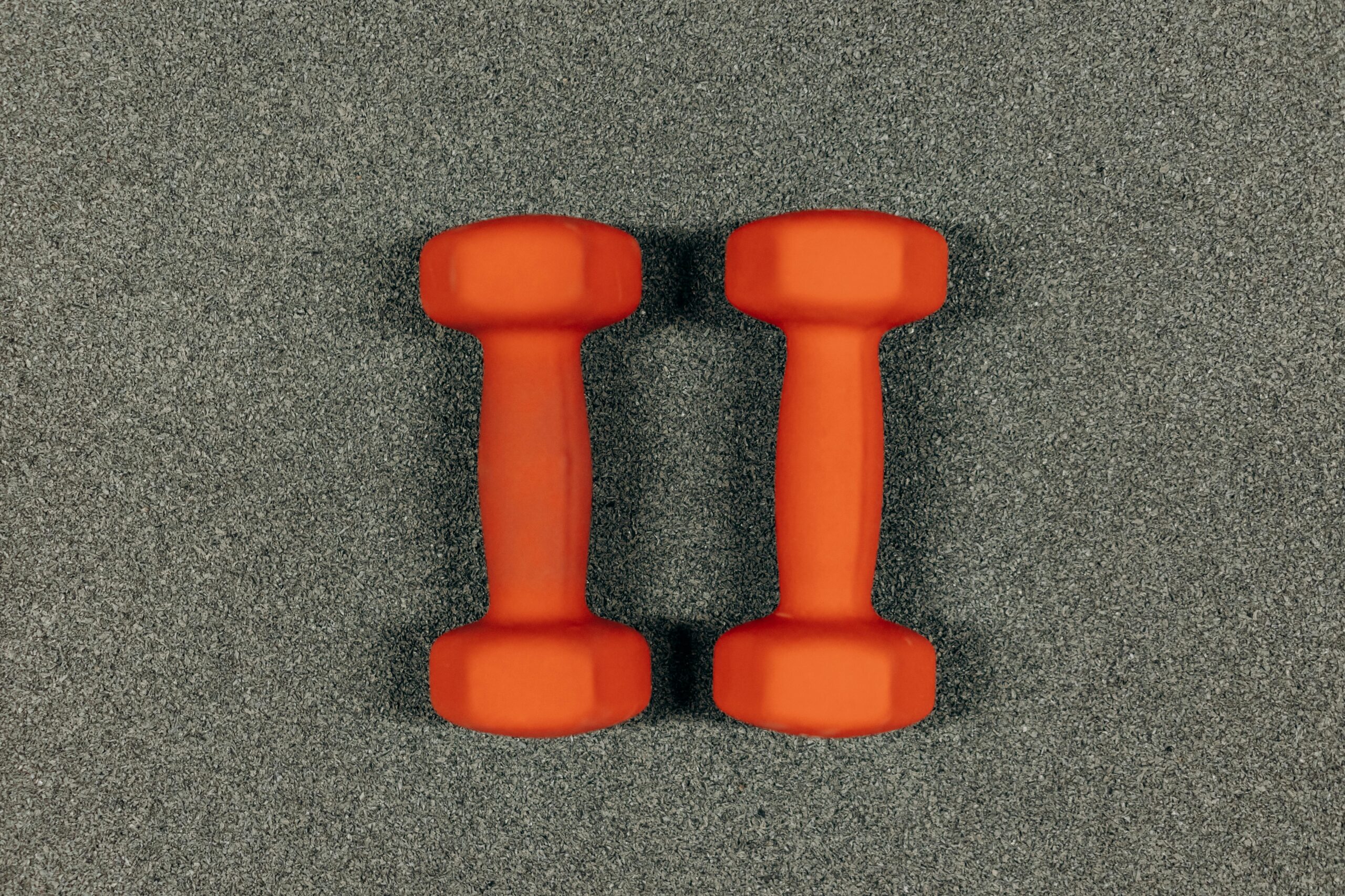 A close-up image of orange dumbbells on a textured gray surface, ideal for fitness themes.